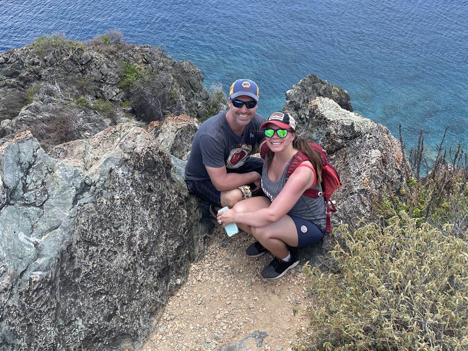 A couple resting on a rocky coastal trail above clear blue water
