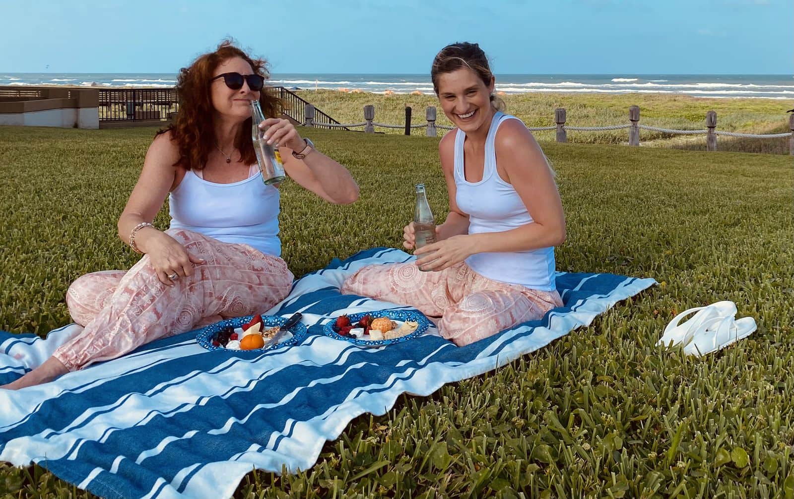 Alicia and a friend laughing over a picnic on a lawn by the sea