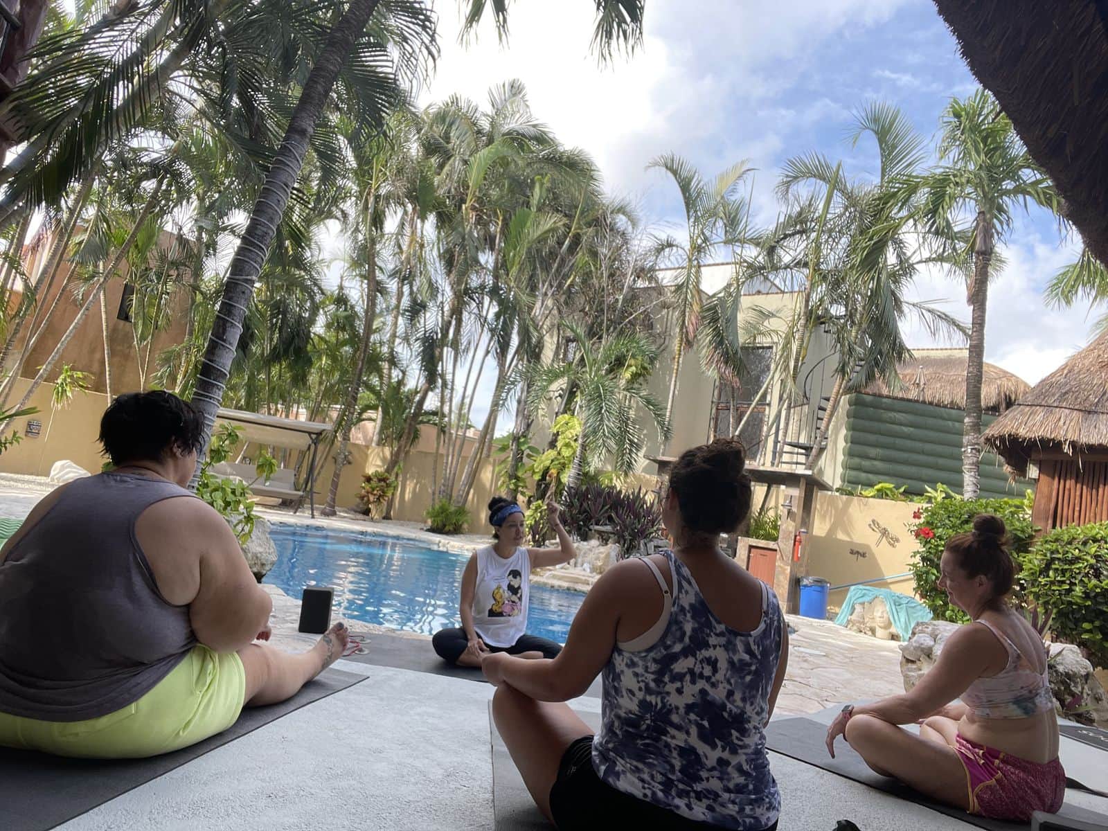 Retreat guests seated on mats in a circle beside a pool under palm trees