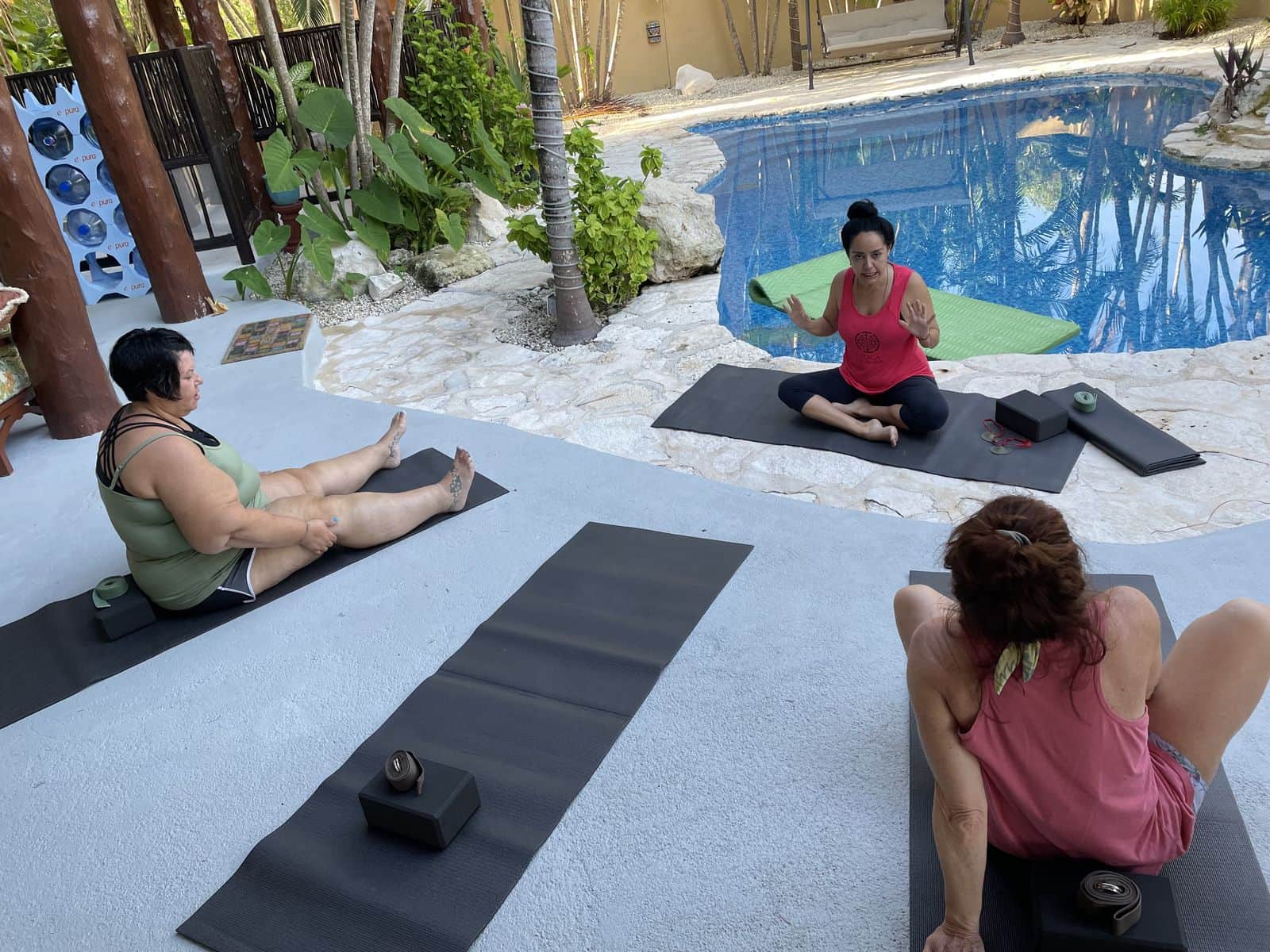 A small group seated on mats for a poolside session at a retreat