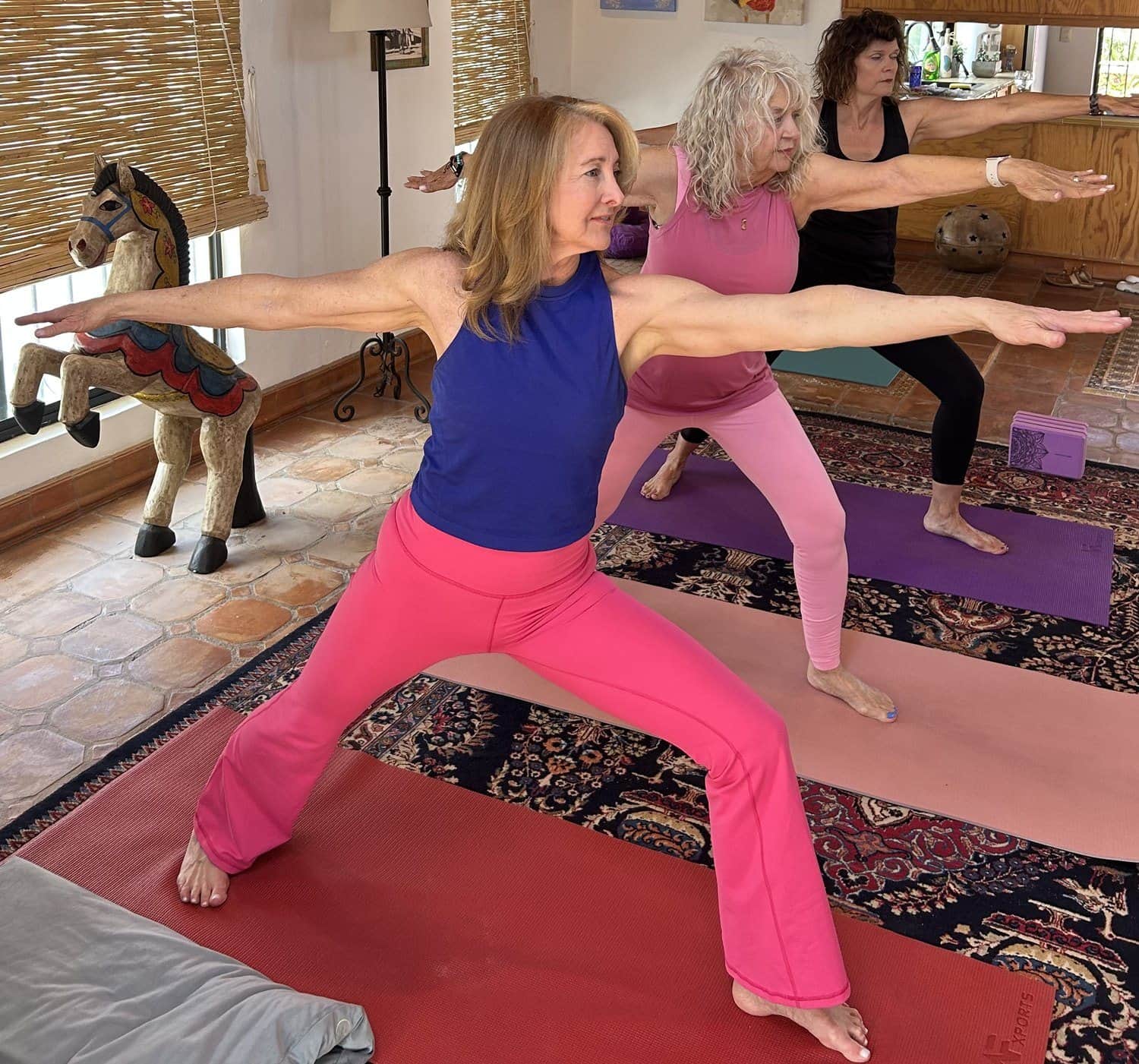 Alicia leading two women in warrior pose in a sunlit studio