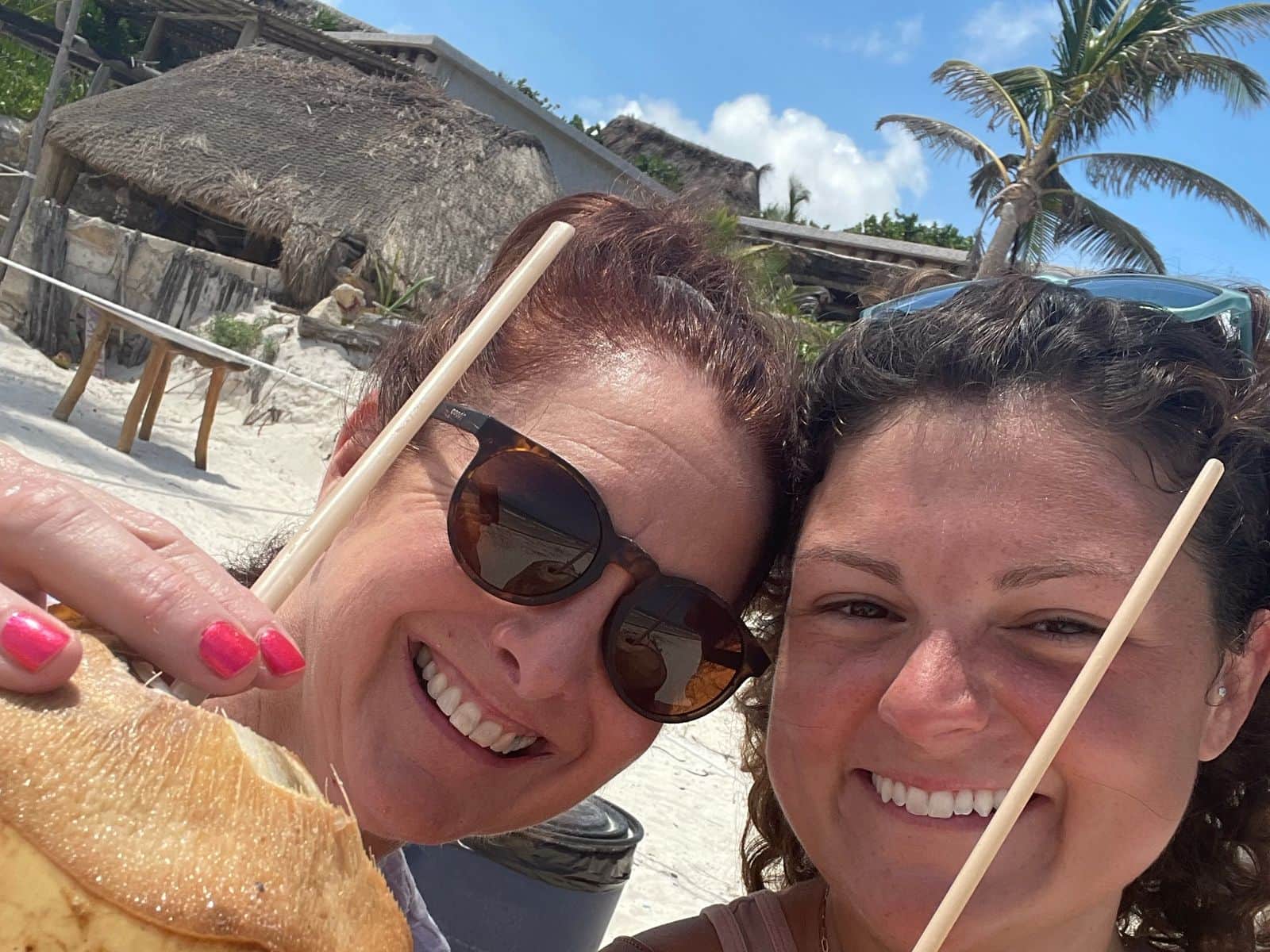 Alicia and a young woman toasting with fresh coconuts on the beach near Tulum